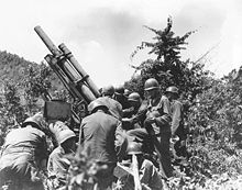 A group of soldiers readying a large gun in some brush.