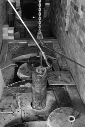 Chainfall and metal flanged, closed cylinder being lowered into a hole