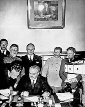 Soviet Foreign Minister Vyacheslav Molotov signs the Molotov-Ribbentrop Pact. Behind him stand German Foreign Minister Joachim von Ribbentrop and Soviet Premier Joseph Stalin.