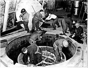 Soldiers and workmen, some wearing steel helmet, clamber over what looks like a giant manhole.